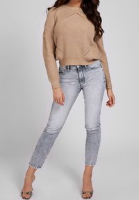 Beige knitted sweater with textured design and open stitches, paired with light wash, form-fitting jeans and strappy heeled sandals.