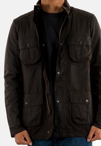 Bruine waterdichte jas met vier voorzakken, drukknoopsluiting en een rits aan de voorkant. Beschikt over een kraag en een gladde textuur.