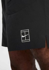 Calções atléticos pretos com um logótipo branco da Nike num retângulo na lateral, feitos de um tecido leve e suave com uma textura subtil.