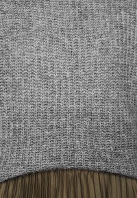 Grau gestrickter Pullover mit geripptem Muster, kombiniert mit einem plissierten olivgrünen Rock. Das Oberteil geht nahtlos in den Rock über.