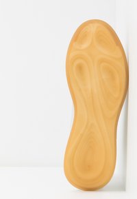 Semelle en caoutchouc avec un motif lisse ondulé de couleur jaune pâle, dotée d'un bout arrondi et d'un bord légèrement relevé pour une meilleure adhérence.