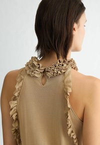 Top marrone con scollatura arricciata e dettaglio a chiave sul retro. Il tessuto ha una texture liscia con una leggera lucentezza.