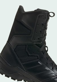 Black tactical boot featuring a mix of textured mesh and smooth leather, with reinforced stitching and a rugged sole for traction.