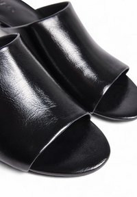 Chanclas negras de material sintético brillante, con punta abierta, tira superior ancha y textura suave. Sin adornos visibles.