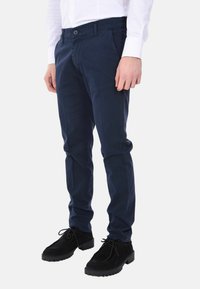 Chino blu navy realizzati in cotone, con una vestibilità slim, tasche laterali e chiusura a bottone. Abbinati a scarpe in suede nere.