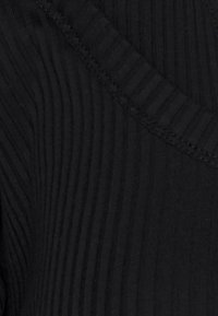 Tissu noir à côtes présentant un motif texturé, avec un subtil col en V et des coutures ton sur ton, mettant en valeur l'élasticité et la flexibilité du matériau.