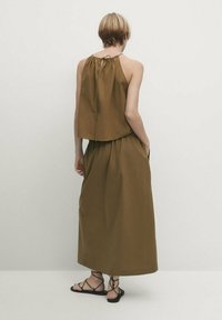 Top marron sans manches et court, ainsi qu'une jupe longueur cheville en tissu l éger ; présente un cordon à nouer à l'arrière. Sandales noires à lanières.