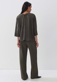 Haut vert olive, ample, avec un dos en V, manches 3/4, associé à un pantalon large assorti et des chaussures noires. Texture lisse.