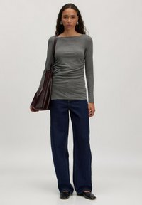 Grijs langemouwen top met zijkanten met plooien, gecombineerd met wijde donkerblauwe jeans. Donkerbruine leren tote bag en zwarte instappers.