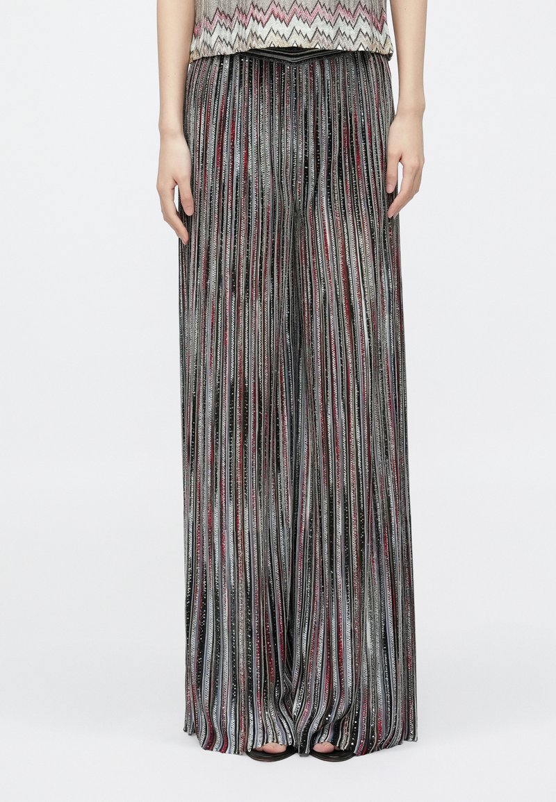 Metszett, széles szárú nadrág fémes anyagból, ezüst, fekete és piros csíkokkal. Puha tapintású, áramló kialakítású.