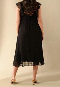 Musta pilkullinen mekko, jossa on röyhelökaulus, liehittyvä helma ja läpikuultavaa kangasta. Yhdistetty kultaisiin korkokenkiin. Sileä rakenne ja kevyt muotoilu.