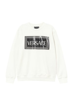 Valkoinen pitkähihainen paita, jossa musta suorakulmainen logotarra rinnassa, jossa lukee valkoisilla kirjaimilla "VERSACE".