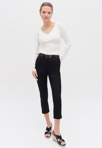 Vit ribbad långärmad topp med V-ringning, ihop med svarta avkortade byxor och svarta kilklack-sandaler med ett kryssband design.