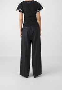 Musta istuva paita, jossa on poimuja ja lyhyet hihat, yhdistettynä löysiin mustiin housuihin, joissa on kaksi taka-taskua ja sileä pinta.