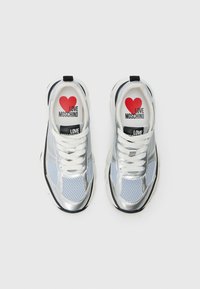 Srebrne mrežaste tenisice za sport s bijelim vezicama, crnim akcentima i otisnutim crvenim srcem kao logom. Na unutrašnjosti tenisica piše "LOVE MOSCHINO".