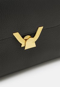 Black textured leather bag featuring a gold metal clasp with a distinctive design. Includes a brand name embossed near the clasp.