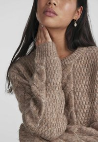 Light brown knitted sweater with a cable pattern, ribbed cuffs, and a crew neckline, made from soft, textured yarn.