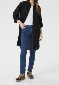 Czarna koszula z guzikami z podwiniętymi rękawami, połączona z niebieskimi slim fit dżinsami i brązowymi sneakersami w cętki. Jednolity kolor, casualowy design.