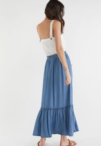 Jupe longue en denim avec un bas évasé et une taille froncée, associée à un haut blanc sans manches avec des boutons aux épaules.