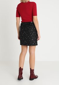 Top rojo de manga corta con ribetes, combinado con una falda negra con estampado. El conjunto se complementa con botines burdeos brillantes.