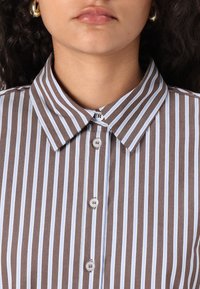 Brown and light blue striped shirt with a collar, featuring white buttons down the front and a smooth, textured fabric.