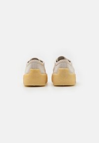 Sneakers in suede beige con una finitura texturizzata, caratterizzati da una particolare suola in gomma gialla e dettagli di cucitura minimalisti sul retro.