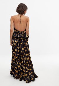 Robe noire longue avec un col halter, un dos ouvert et une taille froncée. Présente des motifs dorés de soleil et de lune sur l'ensemble du tissu.