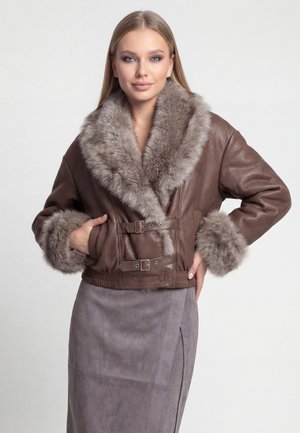 Donna con giacca di pelle marrone con bordo spesso in pelliccia su colletto e polsini, abbinata a una gonna grigia in suede.