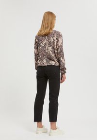 Långärmad, mönstrad blus i beige och bruna nyanser, tillsammans med svarta, högmidjade jeans och vita sneakers, sedd bakifrån.