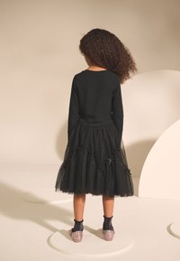 Top nero a maniche lunghe abbinato a una gonna nera in tulle a più strati, con dettagli in nastro. Scarpe scintillanti con un leggero zeppa e calzini neri.