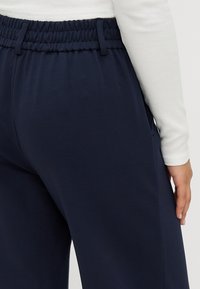 Námořnické modré joggingové kalhoty s elastickým pasem, s hladkým povrchem a bočními kapsami, spárované s bílou košilí s dlouhým rukávem.