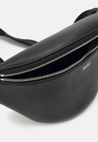 Borsa in nylon nera con superficie strutturata, apertura con zip e marchio impresso. Presenta una forma curvata e una tracolla regolabile.