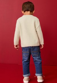 Pull en maille beige clair avec un col côtelé, associé à un jean en denim bleu. Le jean a des ourlets retournés et deux poches arrière.