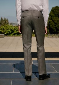 Pantalons gris ajustés en tissu texturé, dotés de deux poches arrière avec des boutons et d'une coupe droite, associés à des chaussures noires.