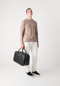 Maglione lavorato a maglia beige, pantaloni bianchi e borsa in pelle nera. La borsa ha una forma arrotondata, manici neri e dettagli in metallo argentato. Sneakers nere.