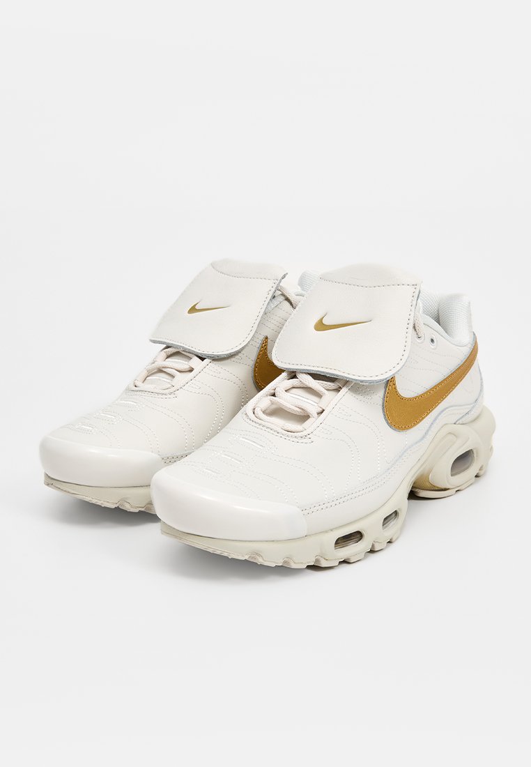 Weiße Leder-Sneaker mit goldenen Akzenten, ausgestattet mit einer gepolsterten Zunge, runder Zehenpartie und Luftpolsterung in der Sohle. Strukturelle Oberflächendetails.