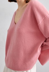 V-Ausschnitt, oversized Pullover aus einem weichen pinken Wollmix; mit überschnittenen Schultern und einem entspannten Schnitt sowie einer glatten Textur.
