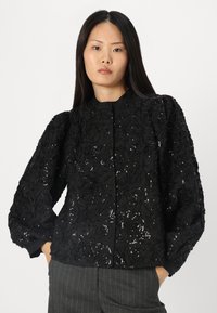 Schwarze bestickte Jacke mit einem strukturierten Blumendesign aus Pailletten, langen puffärmeligen Ärmeln und einem runden Kragen. Kombiniert mit gestreiften Hosen.