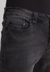 Svart denimjeans med slim fit, standard femfickdesign och subtila uttoningar på tyget nära midjan.