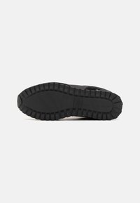 Suela de zapatilla negra con un patrón de goma texturizado, con surcos profundos para mayor tracción. El material es duradero y flexible, diseñado para la comodidad.
