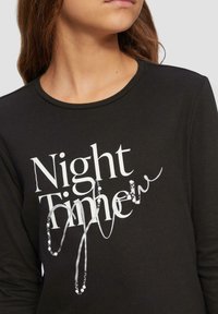 Zwarte langemouwen shirt met de tekst "Night Time" in witte bedrukking en decoratieve accenten in zilver en zwart. Zachte katoen stof.