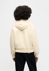 Μπεζ φούτερ με κουκούλα, άνετη εφαρμογή, απαλό ύφασμα και κουκούλα. Διαθέτει ριμπ μανσέτες και τελείωμα. Φοριέται με μαύρο παντελόνι.