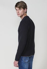 Granatowy sweter z dzianiny z długimi rękawami i okrągłym dekoltem, połączony z niebieskimi dżinsami. Materiał ma teksturowany, prążkowany wzór.