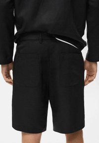 Shorts en lin noir avec une texture lisse, dotés de deux poches arrière plaquées et d'une coupe ajustée. Design simple, sans quincaillerie ou accents marquants.