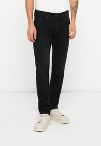 Jeans in denim nero con una vestibilità slim, design a cinque tasche e una finitura leggermente testurizzata, abbinati a sneakers bianche.