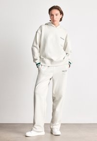 White hoodie and matching sweatpants made of soft fabric. Features a logo on the chest and accents on the cuffs. Simple, relaxed fit.