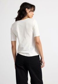 Hvid bomulds t-shirt med korte ærmer, rund halsudskæring og et tætsiddende design. Sat sammen med sorte bukser med brede ben, der har baglommer.