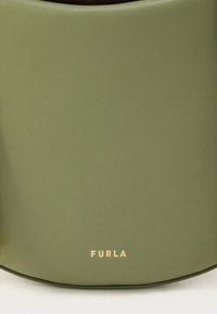 Zaļa ādas soma ar gludu tekstūru, apakšā atrodas zelta "FURLA" logotips. Apaļa forma un minimālistisks dizains.