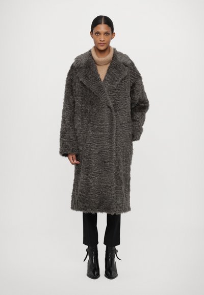 Pilkas dirbtinio kailio paltas su minkšta tekstūra, notch tipo apykakle ir per dideliu siluetu. Dėvimas ant šviesiai rudo megztinio, derinamas su juodomis kelnėmis ir batais.