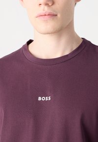 Tmavě fialové bavlněné tričko s kulatým výstřihem, na přední straně s bílým logem "BOSS". Hladká textura s klasickým střihem.